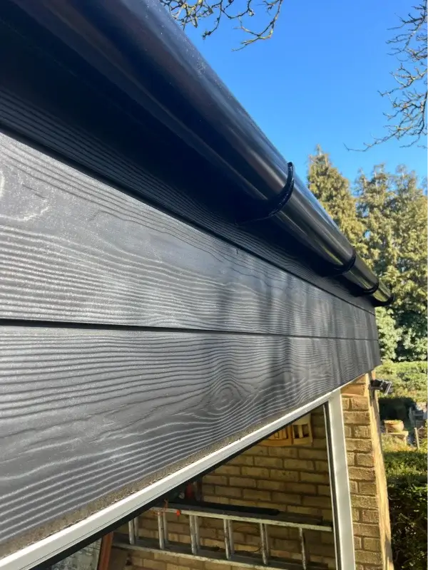 Dark grey horizontal cladding and black guttering fitted above a garage opening. By Norfolk Exterior Solutions.
